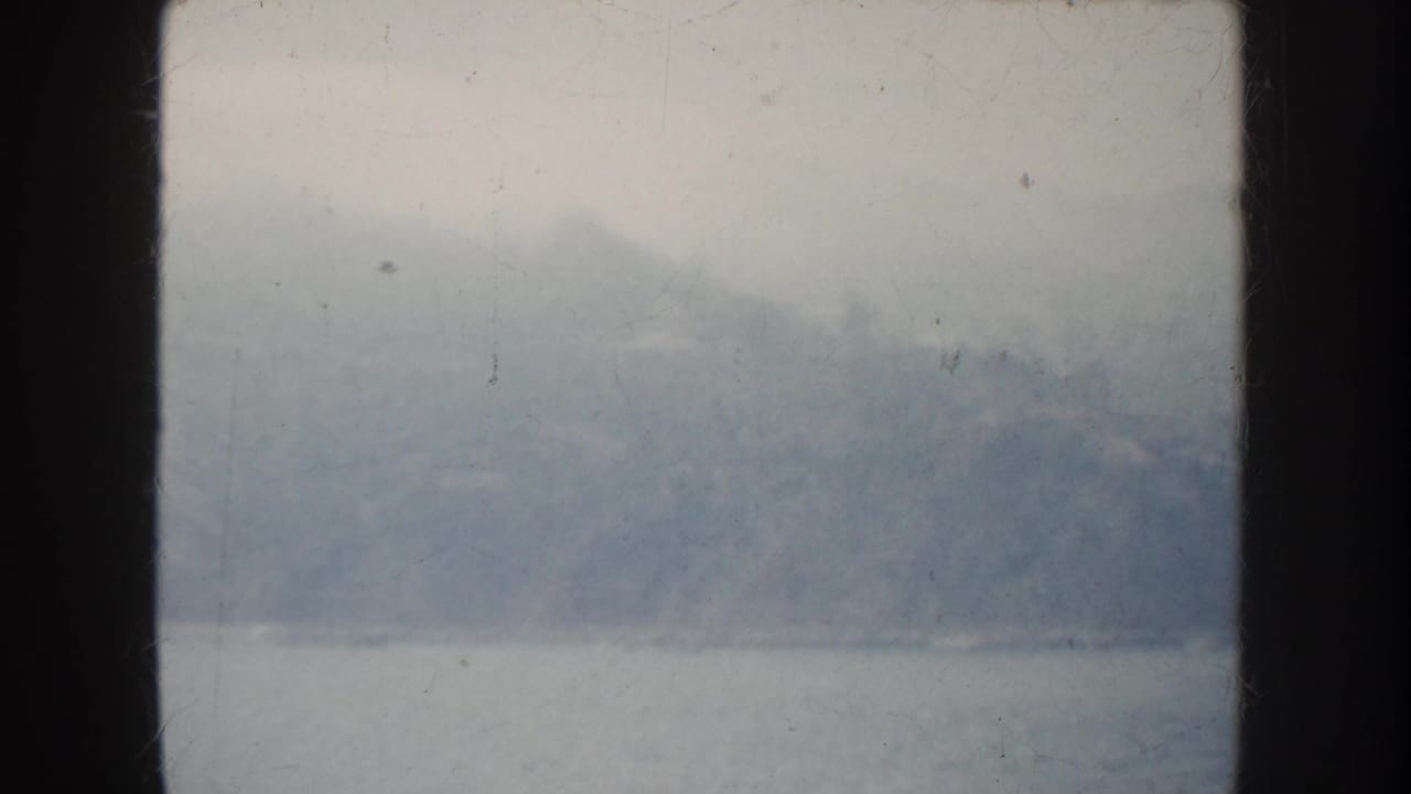 1952 California home-movie frame showing a soft, hazy bay view with distant hills through a dark window frame.