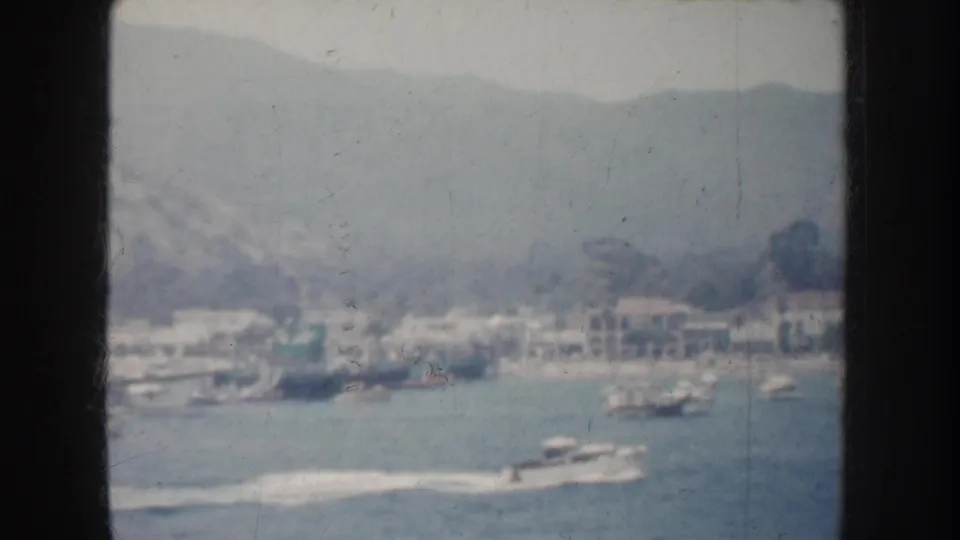 A speedboat crosses a California bay in 1952, leaving a white wake below distant waterfront buildings and hills.
