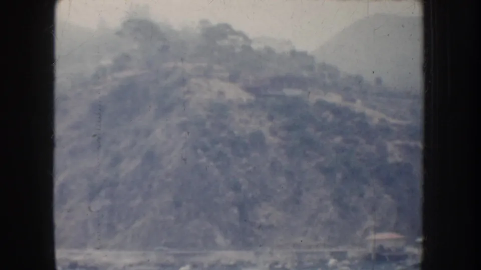 1952 California home-movie view of a hazy harbor hillside, with a possible road or terraced slope above the waterfront.