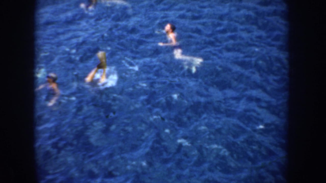 1952 California home-movie frame showing multiple male swimmers spread across dark blue ocean water, viewed from above.