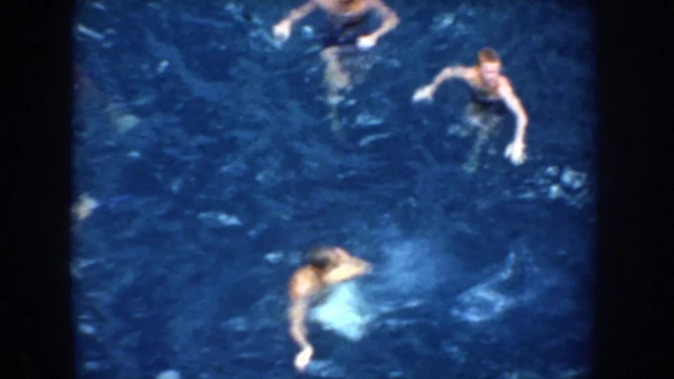 High-angle 1952 California ocean frame showing swimmers separated in deep blue water, softened by motion blur and 8mm texture.