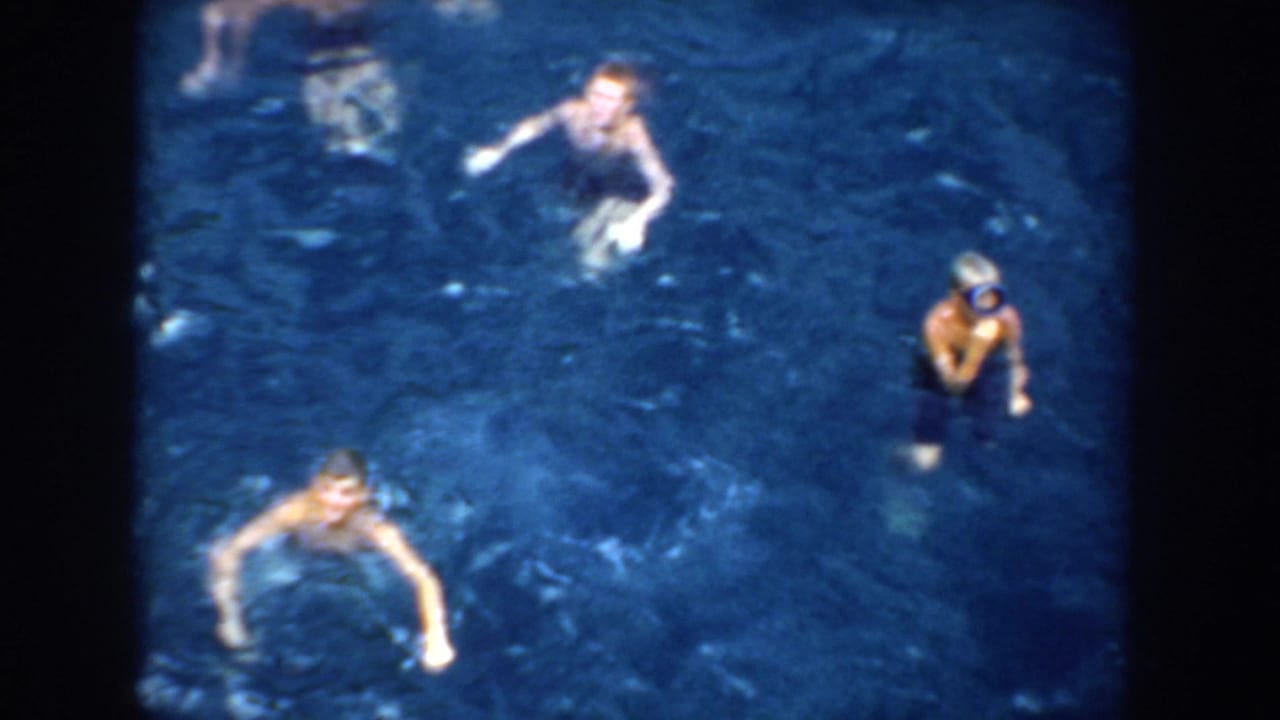 1952 California 8mm frame showing several people swimming in blue pool water from an elevated handheld viewpoint.