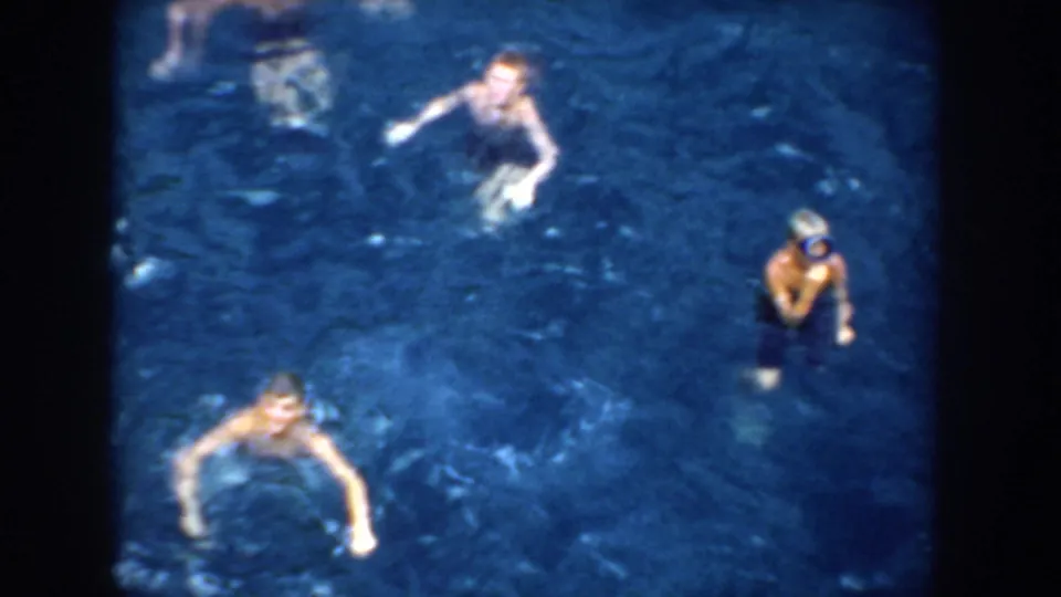 1952 California 8mm frame showing several people swimming in blue pool water from an elevated handheld viewpoint.