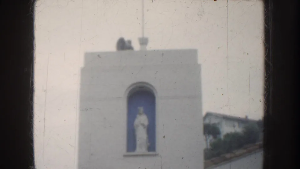 White stucco church structure with an arched blue niche containing a statue, seen in soft 8mm color footage.