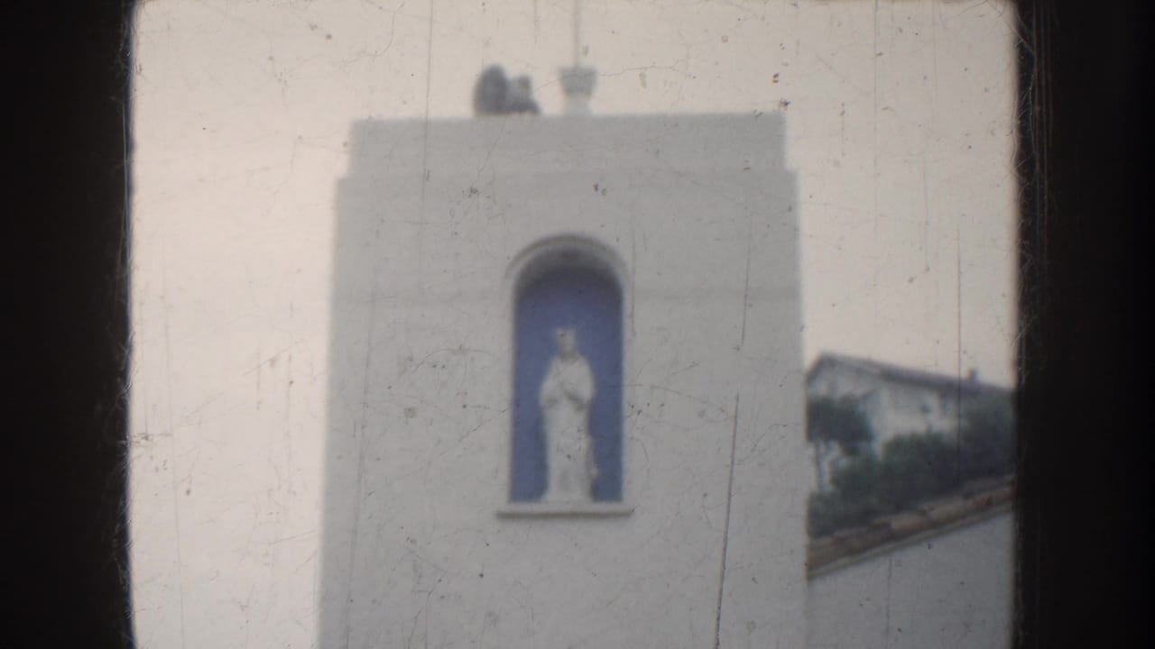 1952 California home-movie view of a white church-like tower with a saint statue in a blue niche, seen through dark framing.