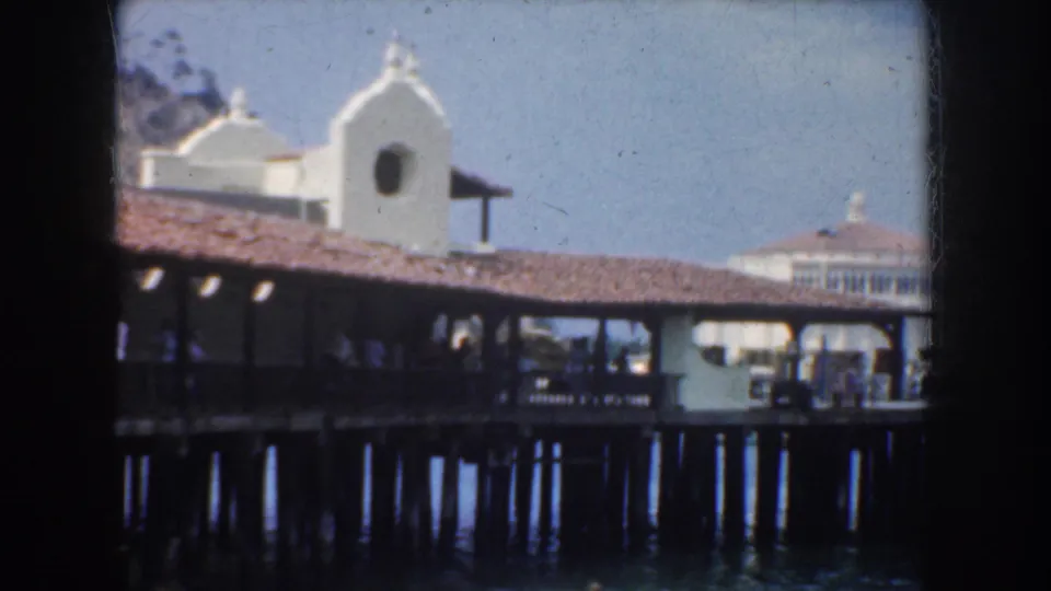 1952 California dockside frame showing a covered pier over water, vertical pilings, and a white tower behind the roofline.