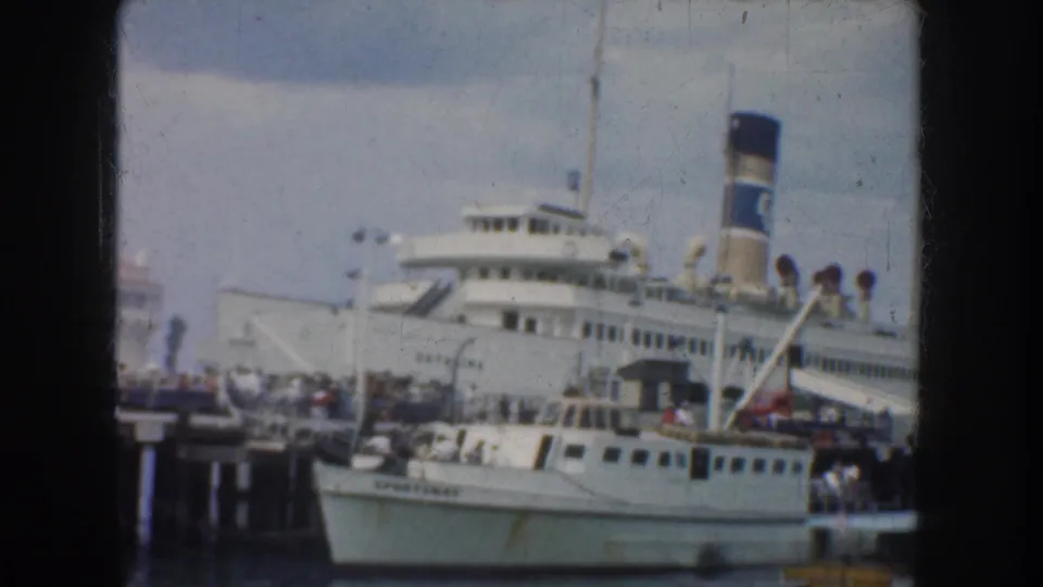 1952 California port scene with a docked passenger ship, visible deck passengers, and a smaller boat alongside the pier.