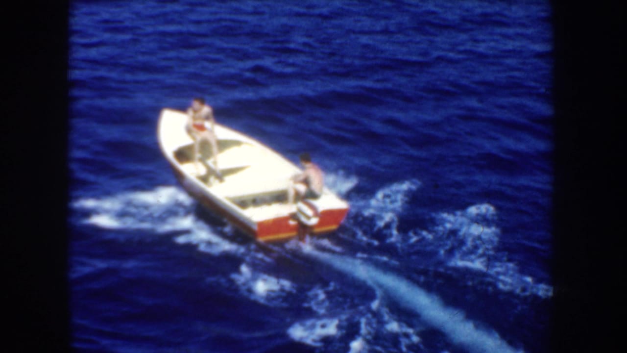 1952 California 8mm footage shows two men in a white motorboat with red trim moving across dark blue ocean water.