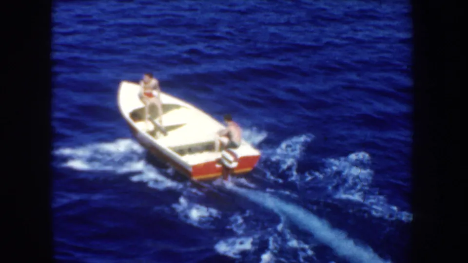 1952 California 8mm footage shows two men in a white motorboat with red trim moving across dark blue ocean water.
