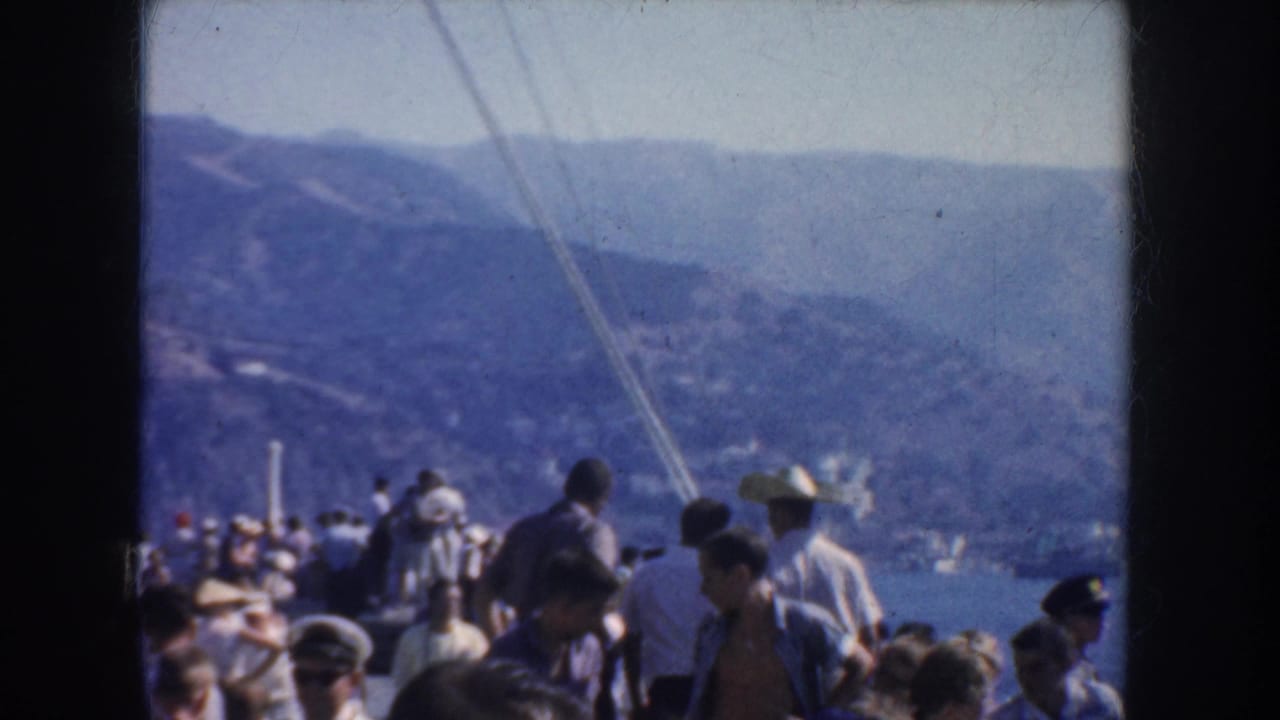 Passengers on a boat deck with cable lines, water, and mountains in the background.