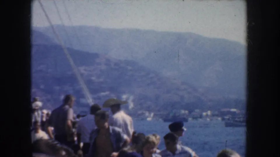 1952 California 8mm still with passengers partly cropped on a sightseeing boat, blue water, distant boats, and hazy mountains.