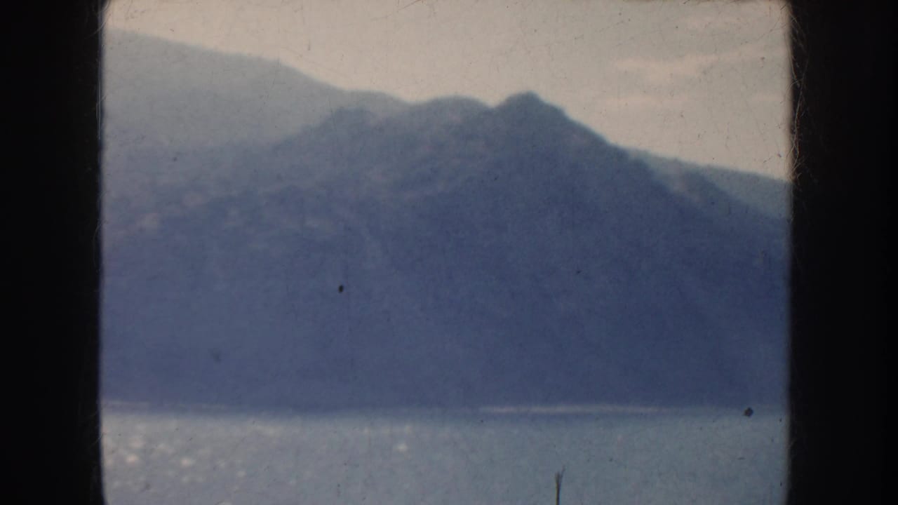 Blue mountain ridge and bright water seen through a dark split film frame.