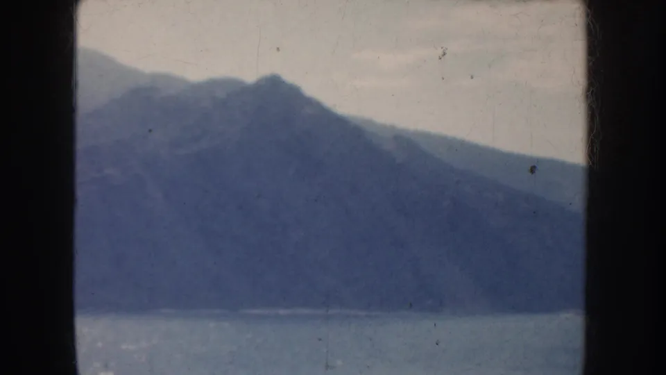 Faded 1952 California 8mm view of a sloping mountain ridge above calm water, with visible scratches and grain.
