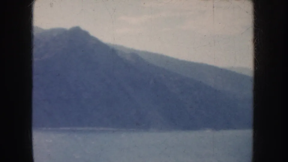 1952 California 8mm frame showing hazy coastal mountains above water with faded color and visible film wear.