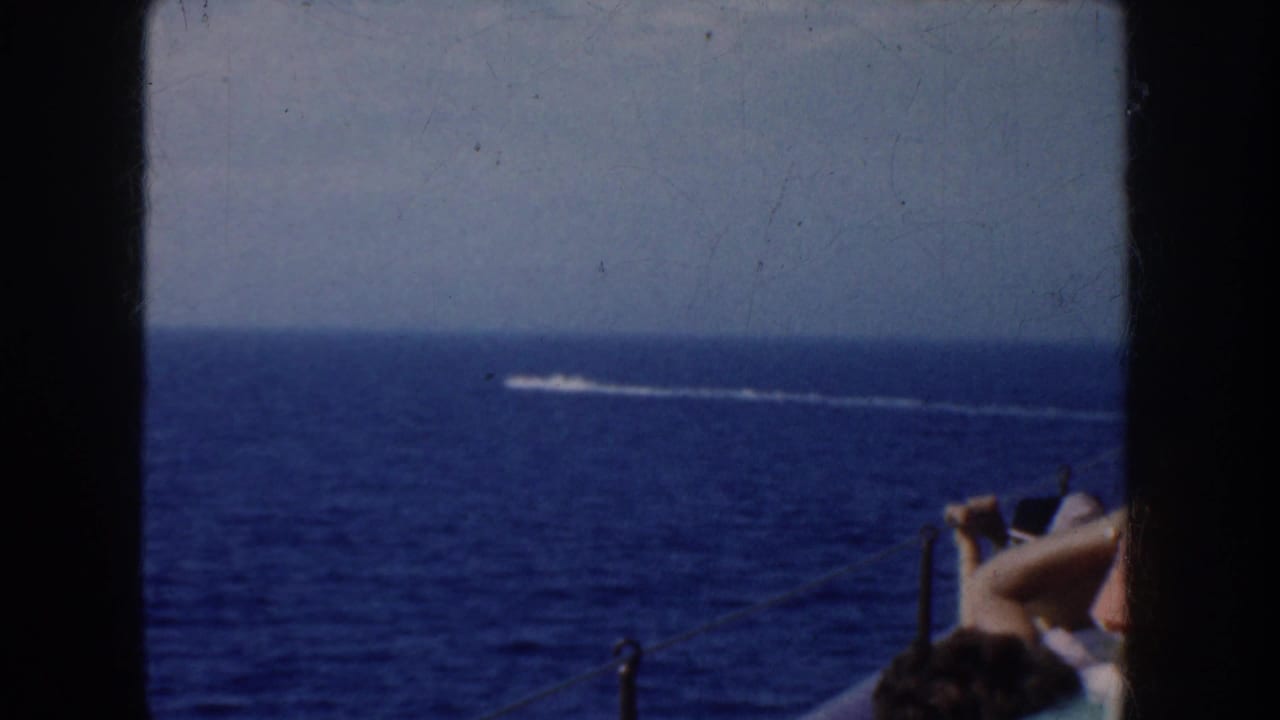 Open blue ocean with a small speedboat wake and partial passengers at the right edge.