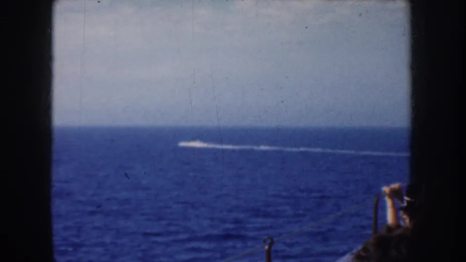 1952 California home-movie frame with a small speedboat and long white wake crossing blue water beyond dark window dividers.