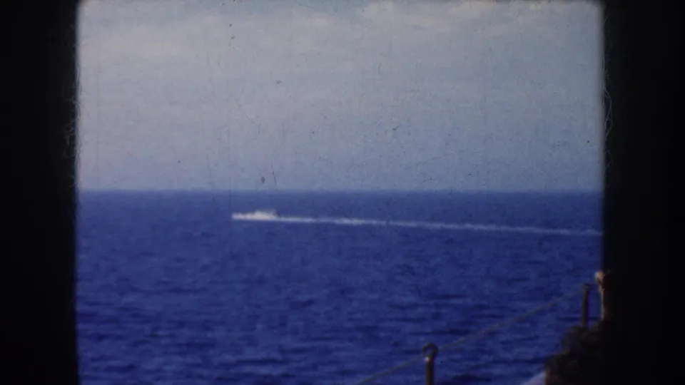 1952 California ocean view showing a distant speedboat wake, pale sky, and a partial passenger near the right frame edge.