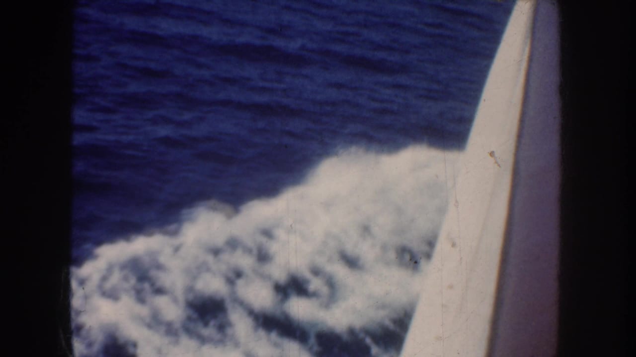 8mm home-movie view from a boat, with the vessel edge at right and white wake spreading across blue ocean.