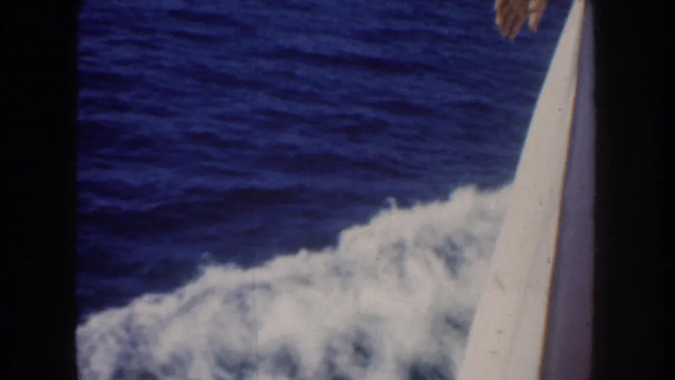 Handheld 1952 boat-view frame showing blue water, foamy wake, boat edge, and a passenger hand entering near the top.