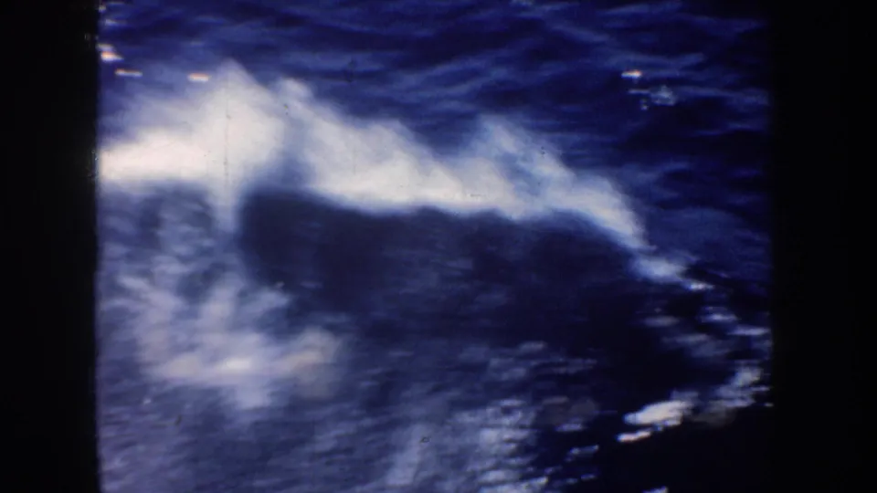 8mm frame of white boat wake spreading across dark blue ocean, with no identifiable vessel details in this view.