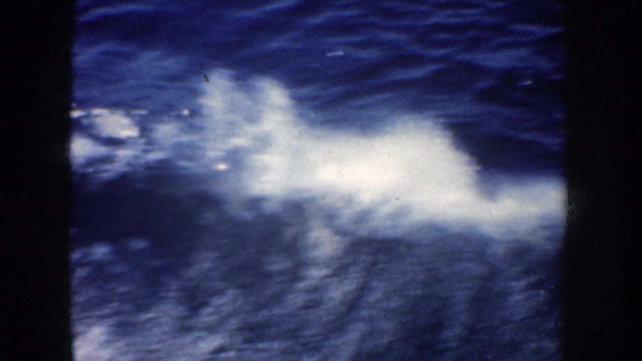 White spray spreads across dark blue water behind a vertical frame bar.