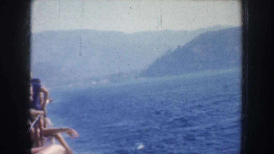 1952 California 8mm frame showing blue water, hazy hills, distant shoreline, and partially visible boat passengers near the rail.