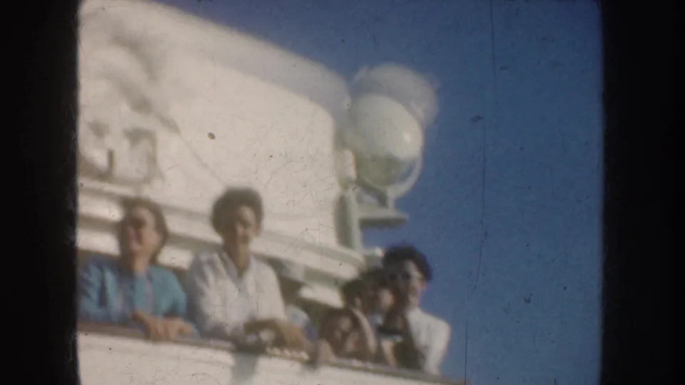 1952 California 8mm frame showing adults on a vessel deck, with a white ship structure and wheel emblem partly visible above them.