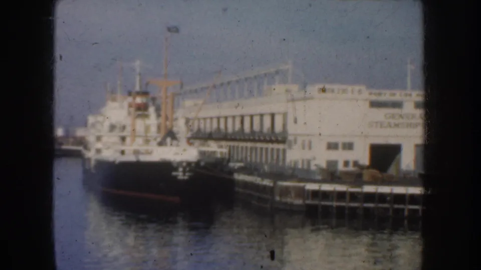 1952 California harbor frame showing a docked vessel, pier, and large building with partially legible steamship signage.