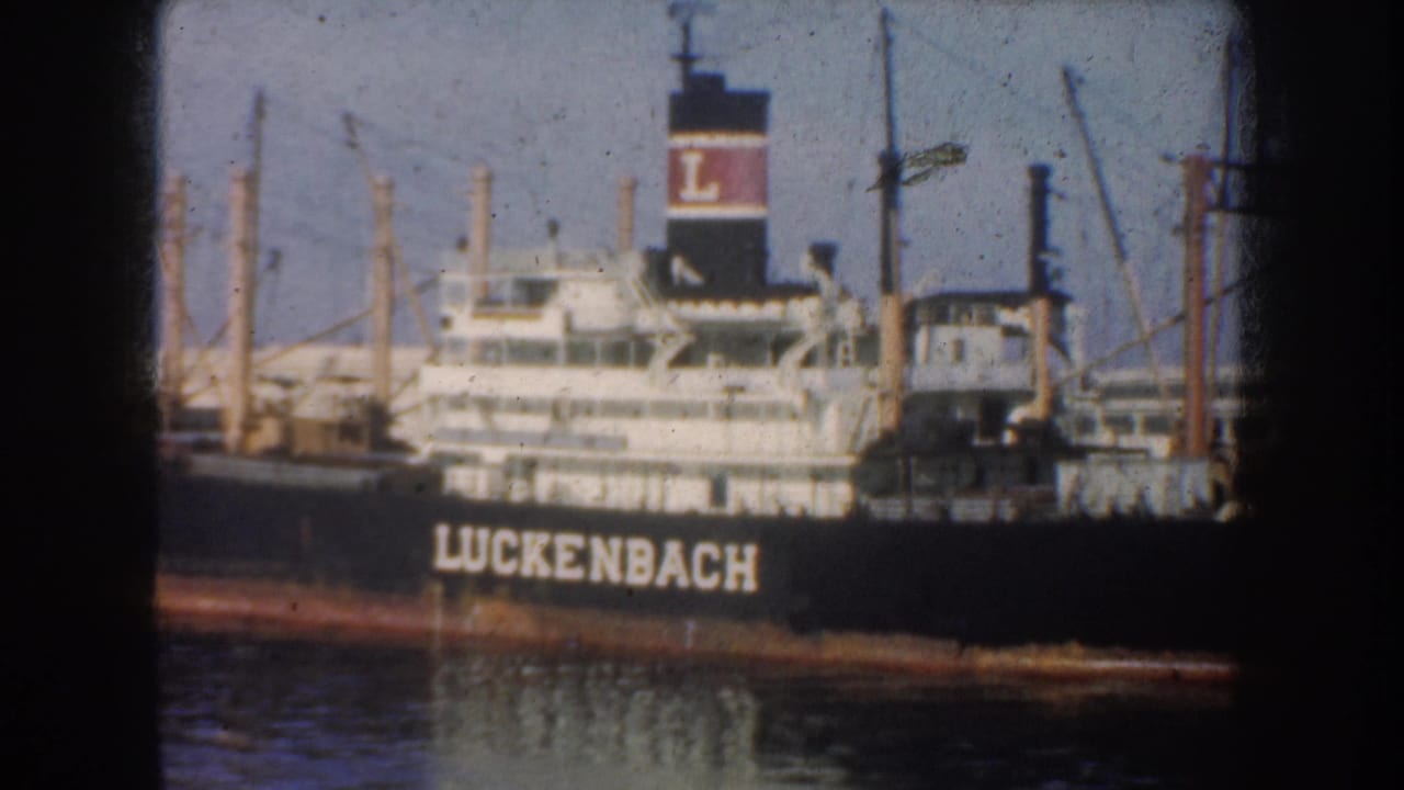 1952 California harbor footage showing the Luckenbach name on a docked cargo ship, with cranes and masts behind it.