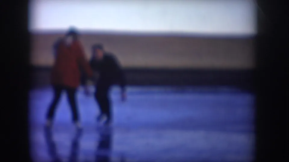 Two adult skaters pass nearer the camera on a frozen North Dakota lake, with another small figure visible farther behind them.