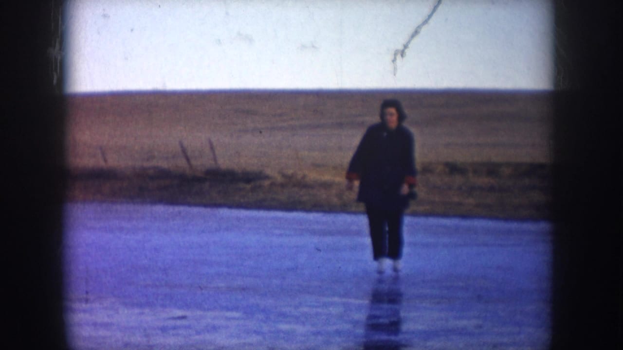 A skater in dark winter clothing appears on a frozen North Dakota lake, with flat open fields and pale sky in the background.