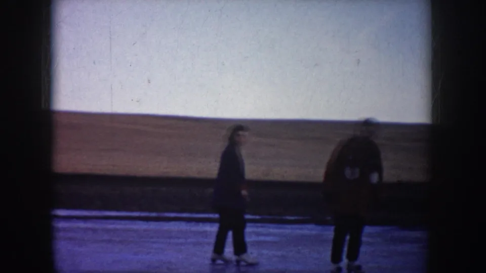 Two people are visible on the frozen lake, one nearer the camera and one farther left, in a rural North Dakota winter setting.