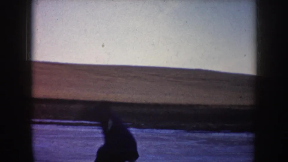 Soft 8mm frame from North Dakota showing a person low on the frozen lake surface against an open winter horizon.