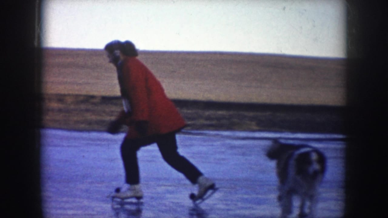 In 1953 North Dakota home-movie footage, a person in a red coat skates across a frozen lake or pond while a dog runs close by.