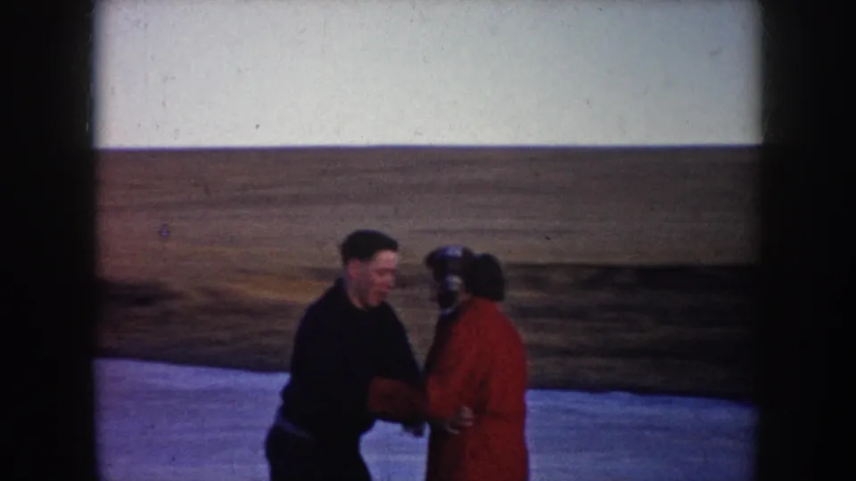A man and woman skate close together on a frozen pond, framed by open North Dakota grassland in the background.