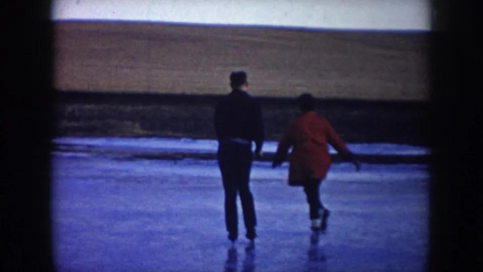 The couple skates away across the frozen lake in a 1953 North Dakota home movie, with a low field horizon ahead.