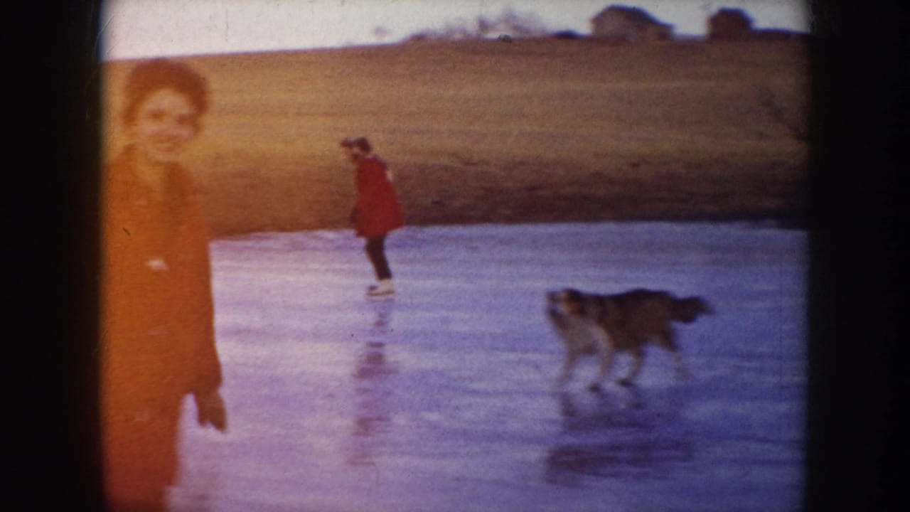 1953 North Dakota home-movie frame showing people skating on a frozen lake while a dog moves across the ice.