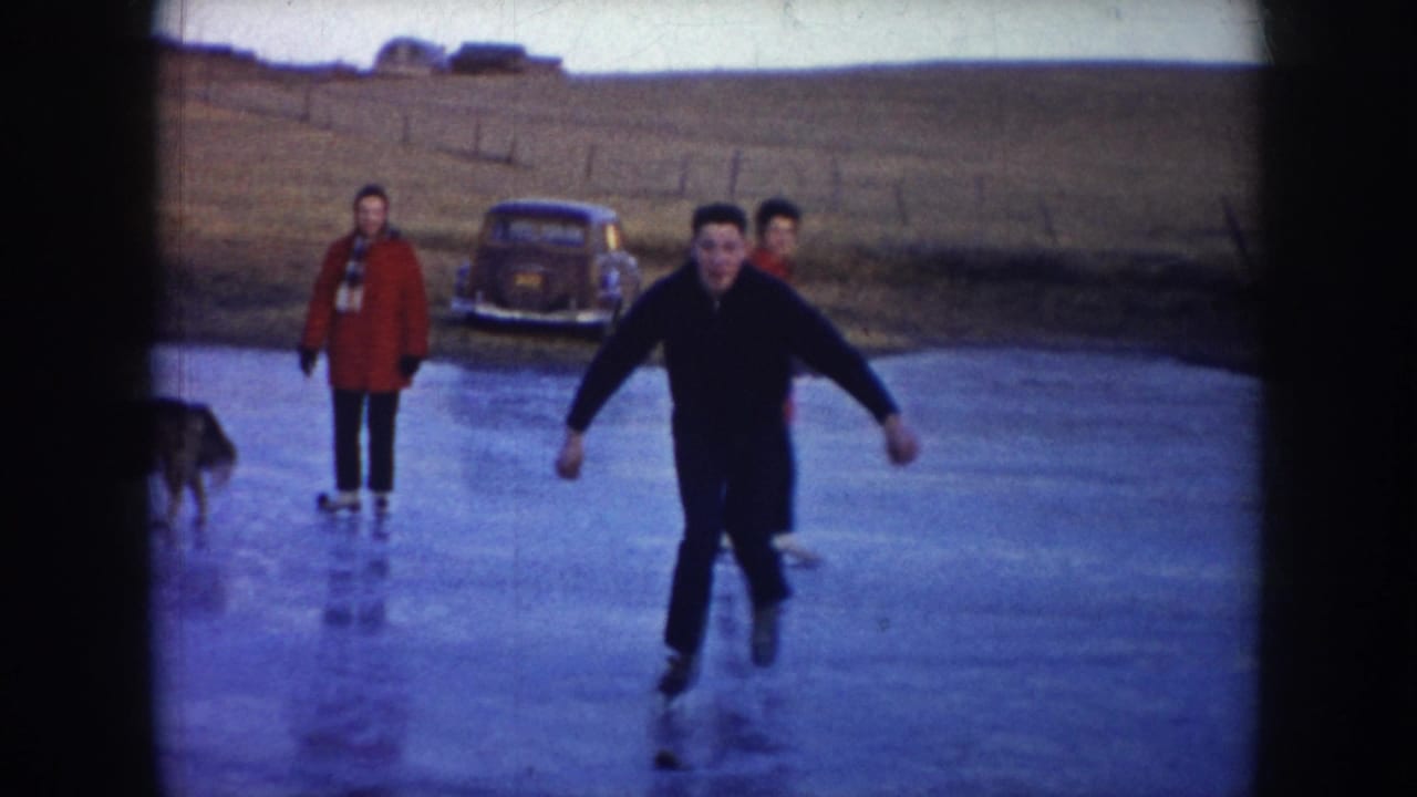 1953 North Dakota home-movie frame showing adults skating on a frozen pond, with a vintage car on the bank and open rural fields beyond.