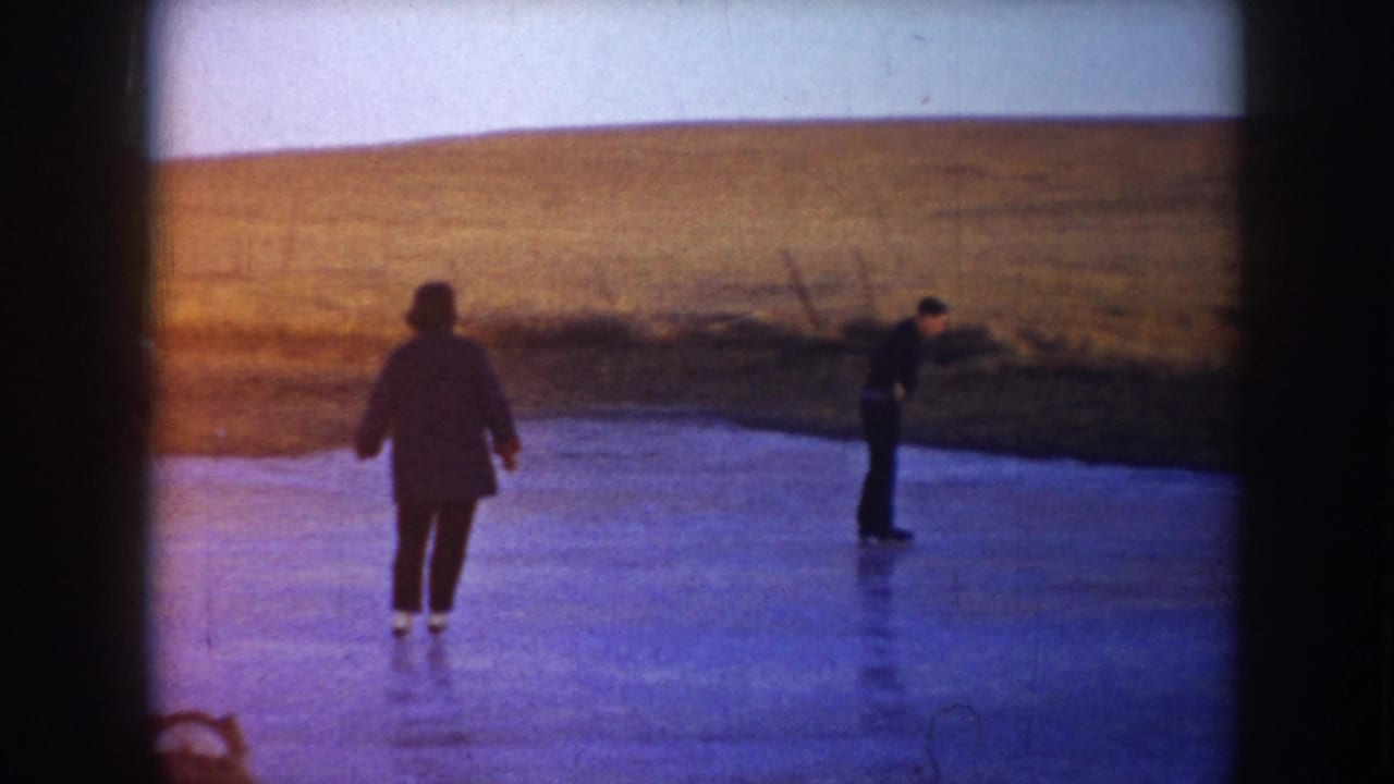 Two people skate on a frozen pond in the metadata-supported 1953 North Dakota rural landscape.