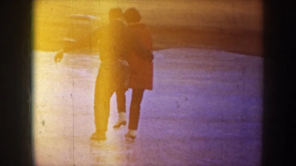 1953 North Dakota 8mm frame showing two adults together on outdoor ice, partly obscured by yellow exposure flare.