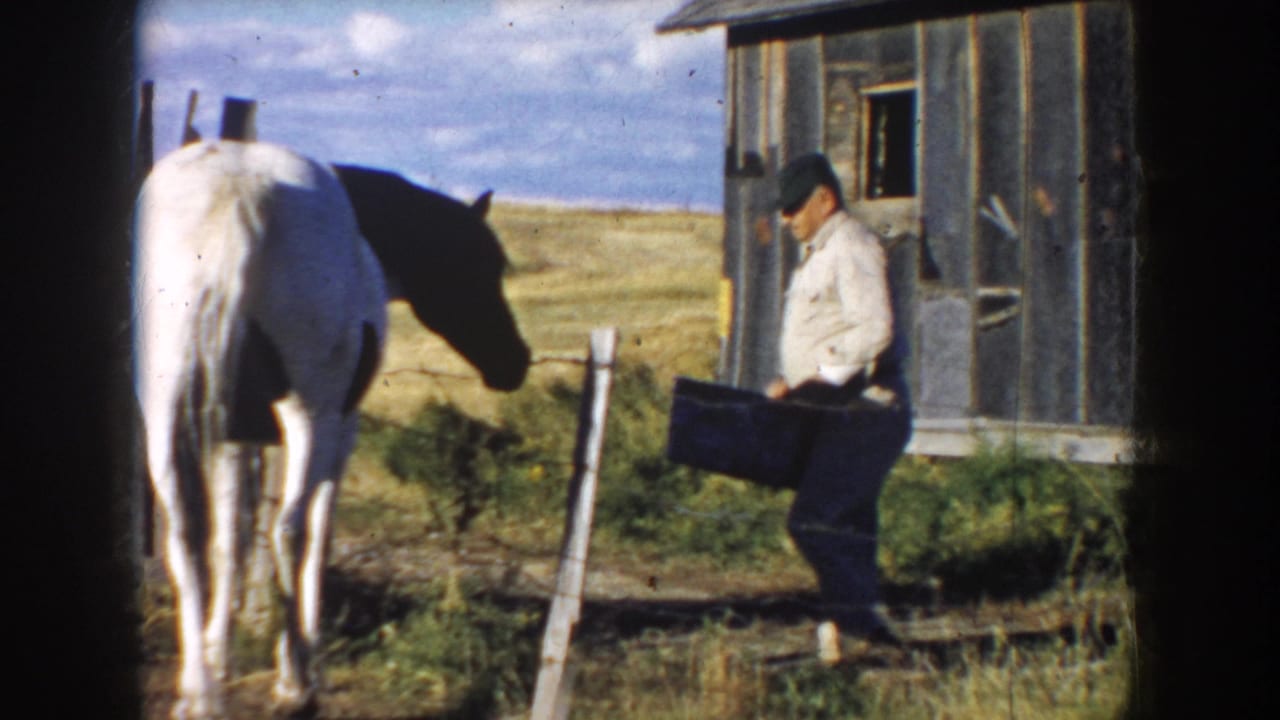 1953 South Dakota 8mm frame showing a farmer with a bucket beside a white horse near a weathered wooden barn and open pasture.