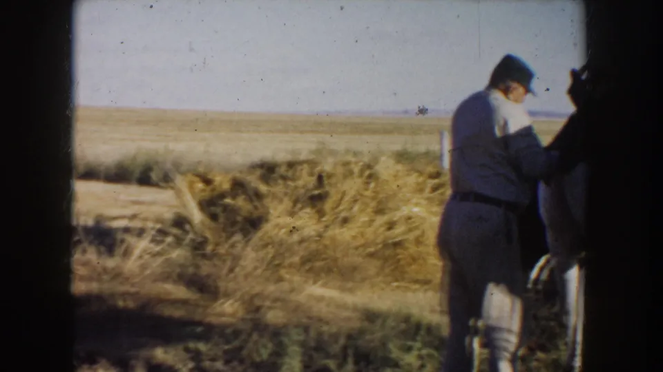 A soft 8mm frame shows the man beside the horse, partly obscured by the film gate, with dry grass and open plains visible.