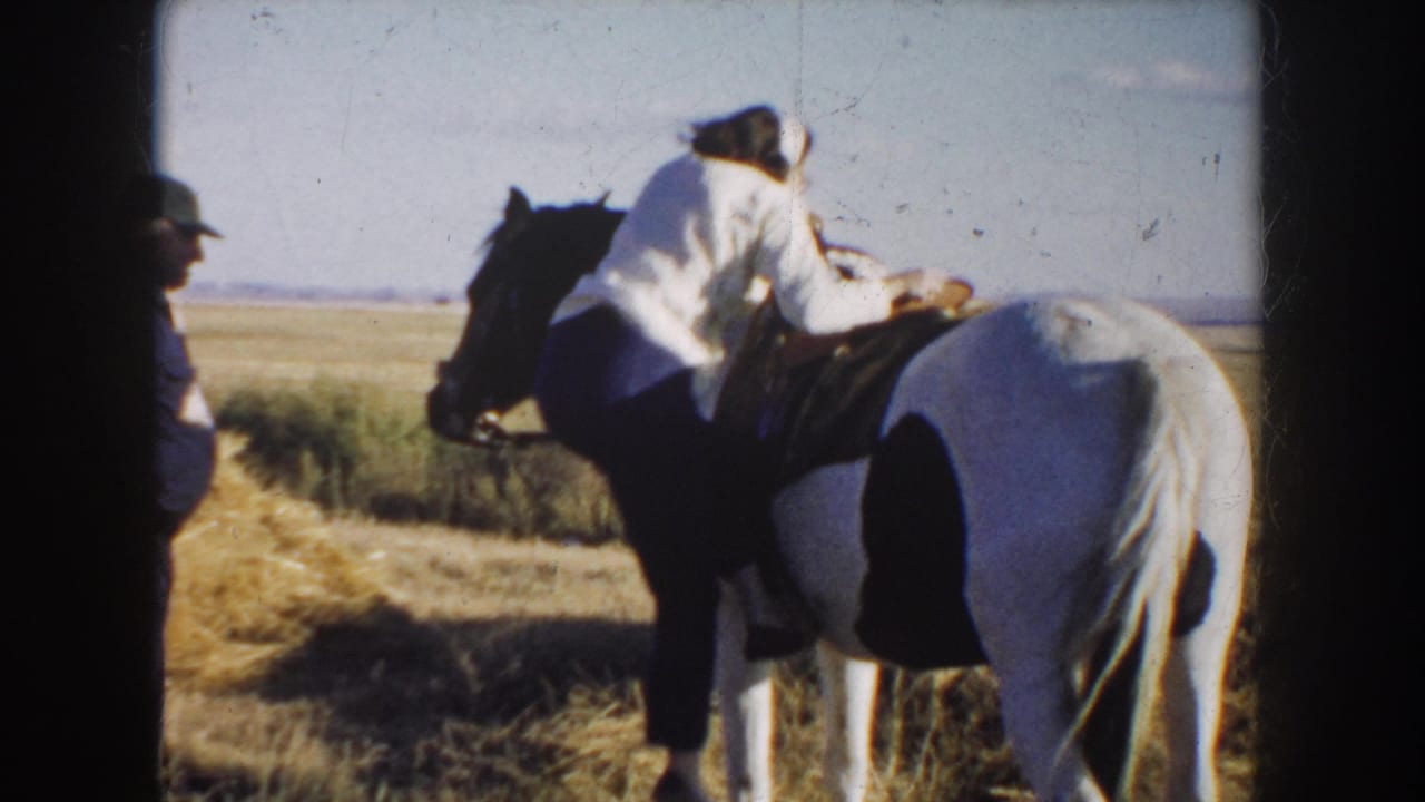 In South Dakota 1953 home-movie footage, a woman in a light blouse climbs onto a saddled pinto horse in an open field.