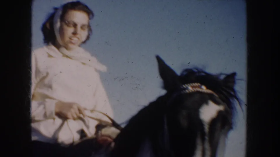 A closer 1953 home-movie frame shows the woman rider holding reins, with the horse's head partly filling the foreground.