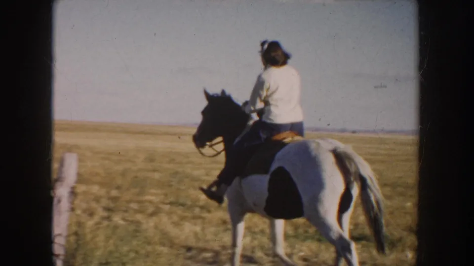 The rider moves away on the pinto horse across the South Dakota field, with fence posts and open prairie visible.