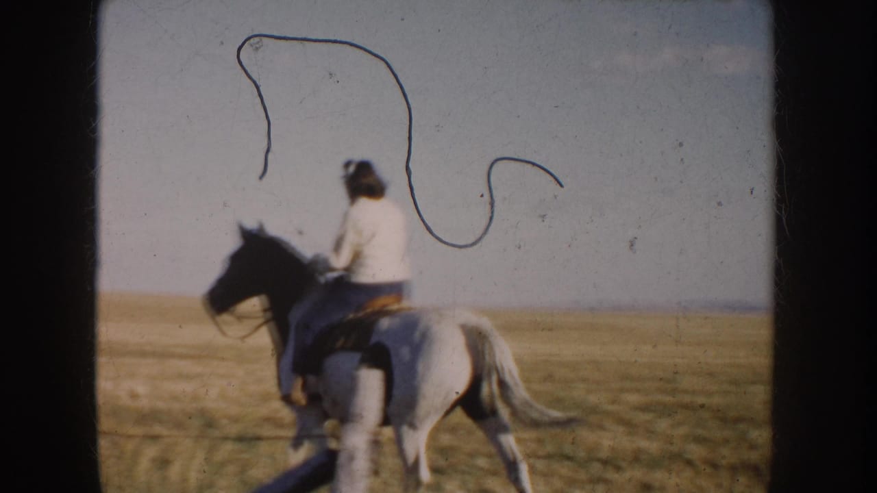 Rider on a black-and-white horse moving across open prairie near a fence line.