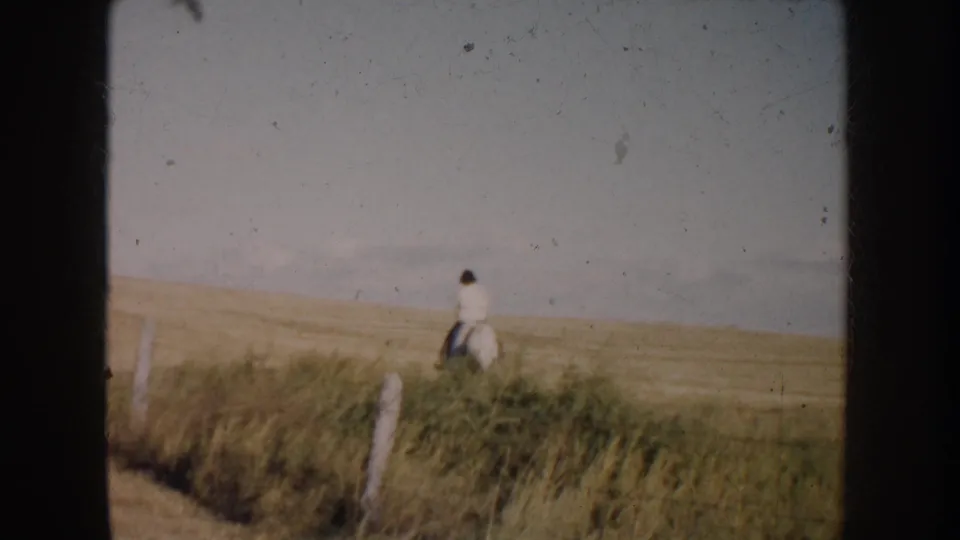 Final 1953 South Dakota frame with the rider and horse far across prairie grass near a simple fence line.