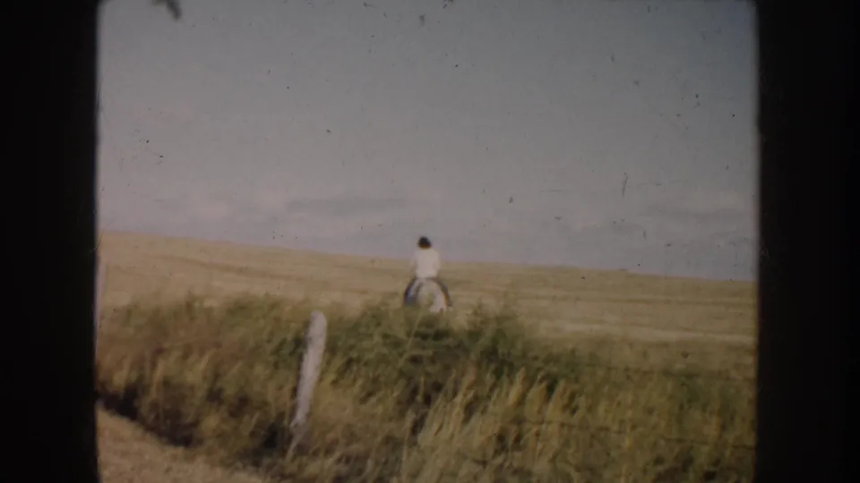 1953 South Dakota 8mm frame showing a distant rider on a black-and-white pinto horse in open prairie pasture.