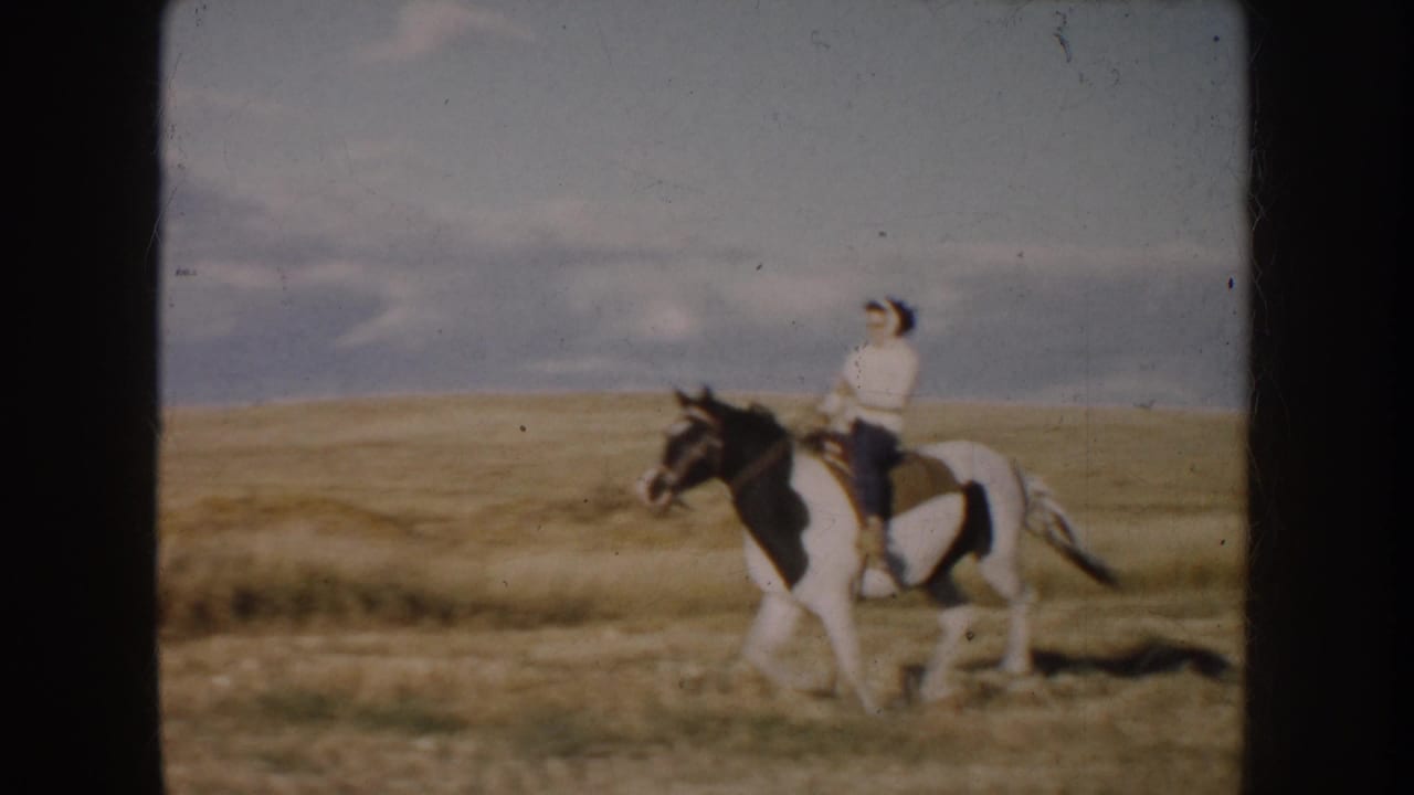 1953 South Dakota 8mm frame with a closer side view of a rider on a black-and-white pinto horse in prairie pasture.