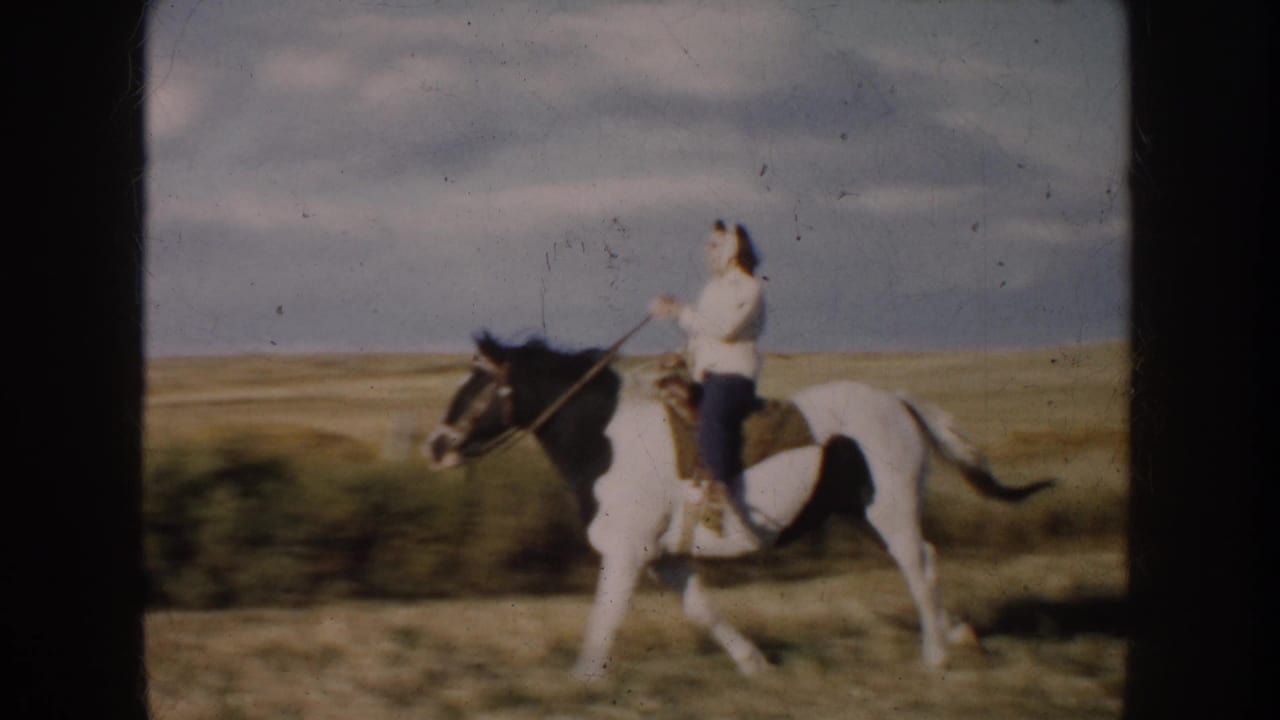 1953 South Dakota 8mm frame showing a rider on a black and white pinto horse crossing an open grass field.